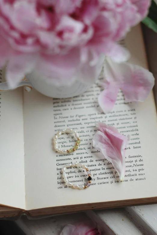 pink flowers are in the background on a book with a pearl ring