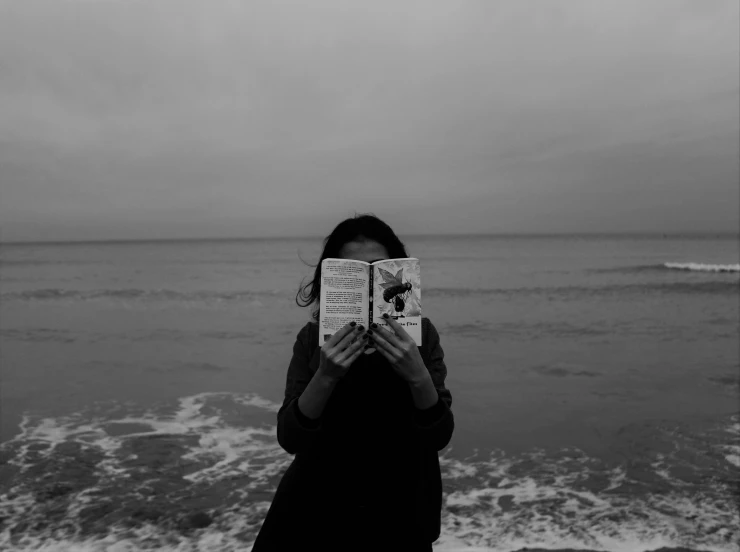 a woman is standing near the ocean reading a book