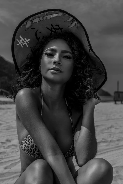 an african american woman sits on the sand in her bikini and hat