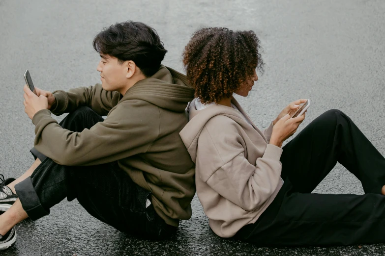 a young couple are sitting on the street looking at their cellphones