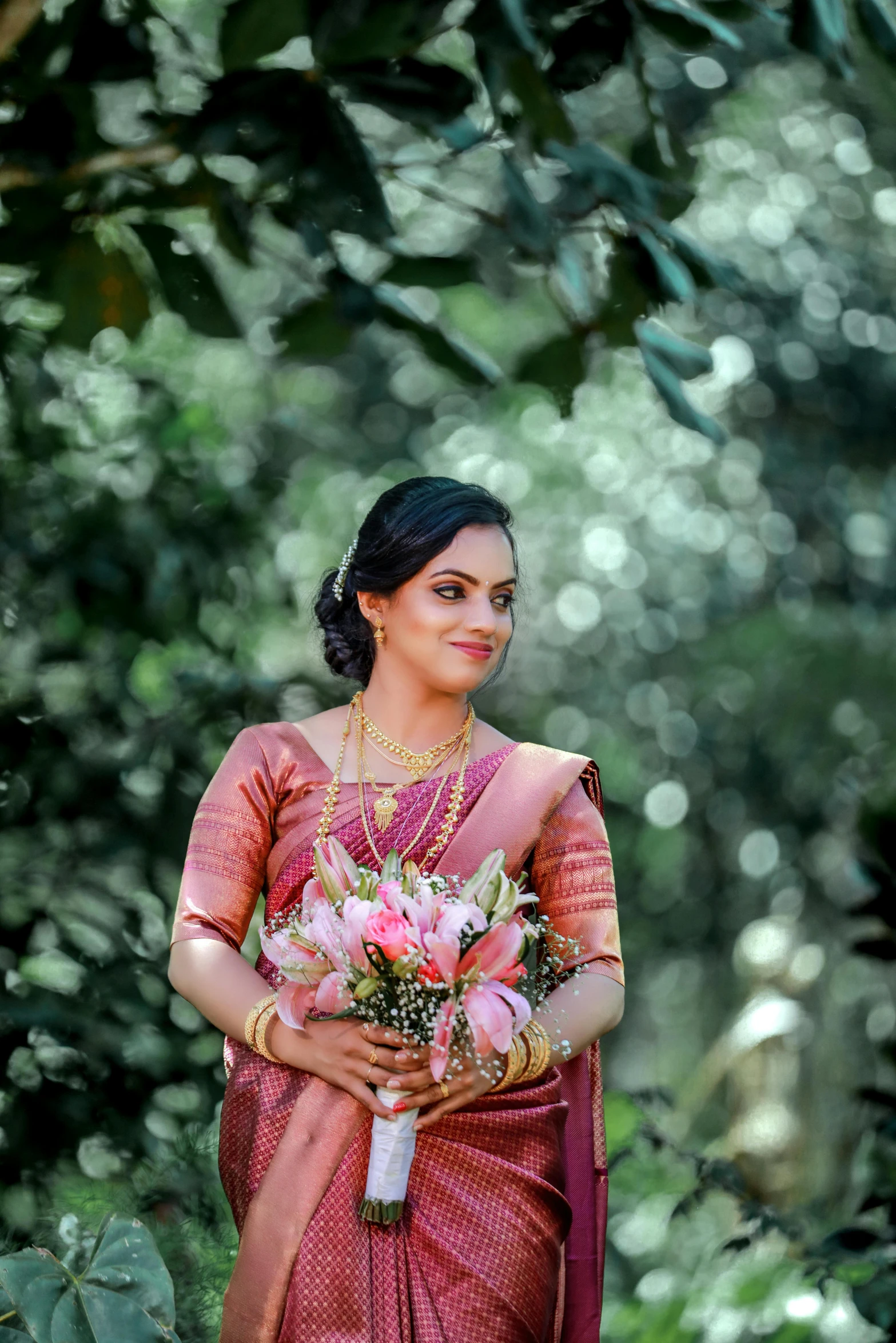 a woman stands near some greenery holding her bouquet
