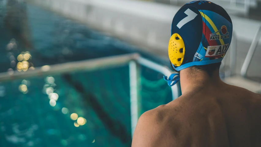 a man with a swim helmet and goggles at the top of a railing looking out onto a swimming pool