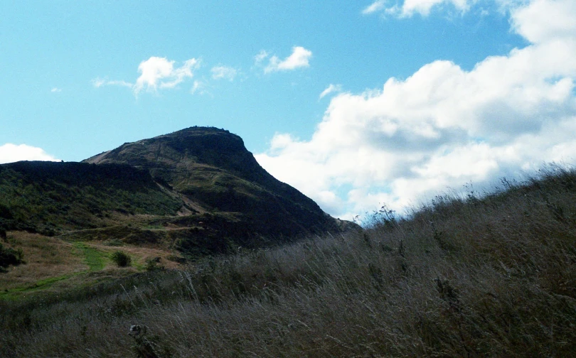 the grass field is under the tall mountain