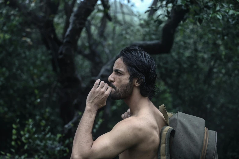 a young man standing in a forest with his shirt on