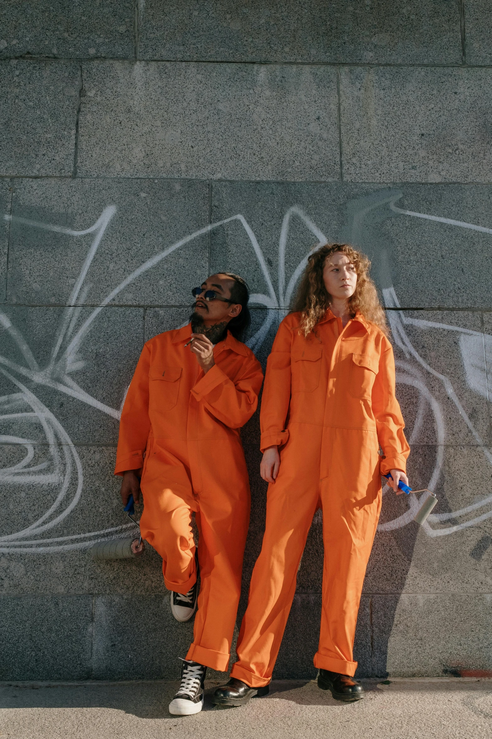 two people in orange jumpsuits, standing against a wall