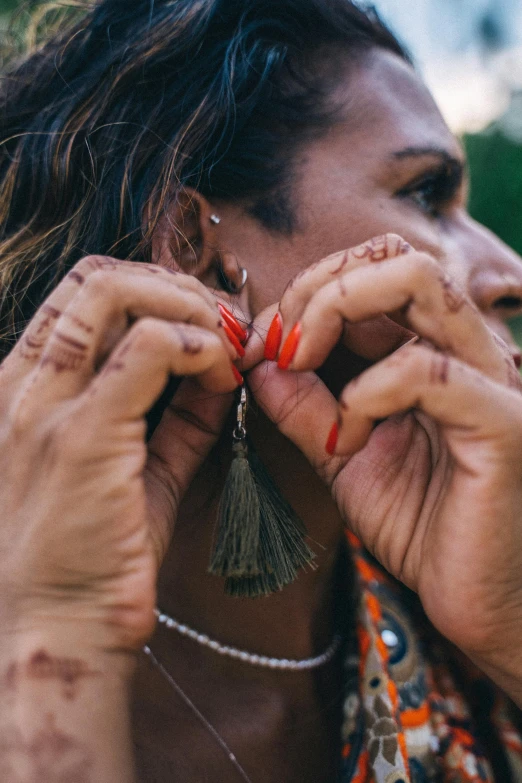 a woman with red nail polish and piercings holding her hand in front of her face