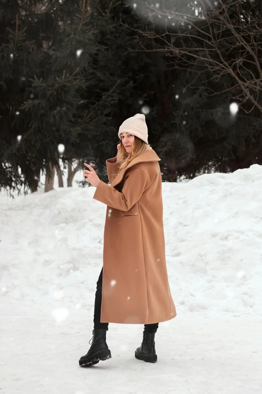 a woman in a long brown coat is standing in the snow