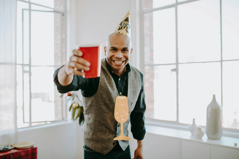 a smiling man wearing a party hat holding a cell phone
