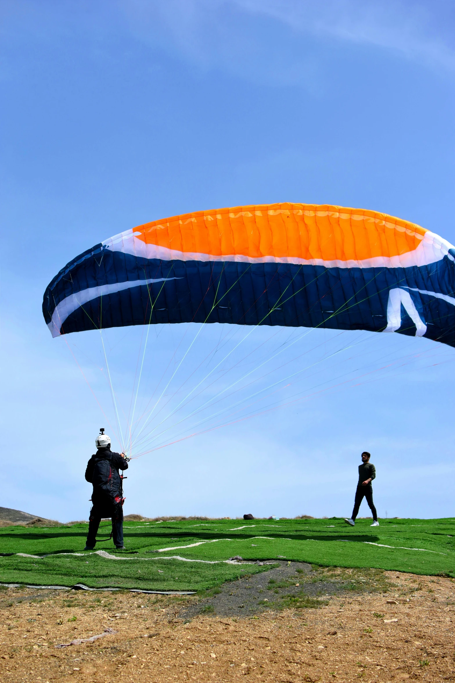 two people on a hill flying an orange and blue parachute