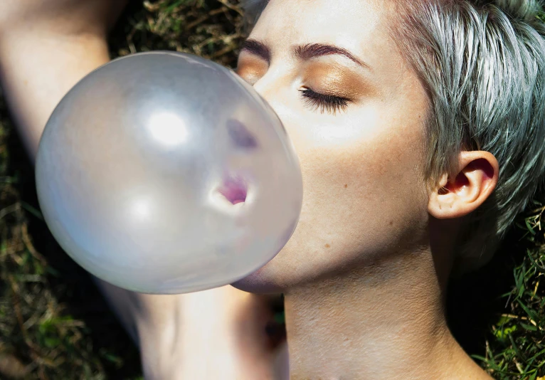 a woman is laying down while blowing a bubble
