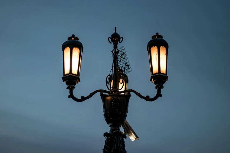 three lamps are lit up against the evening sky