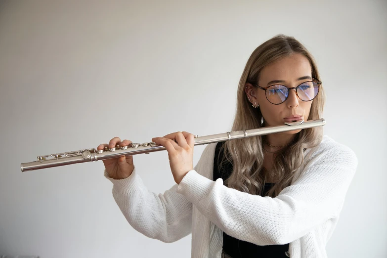 a woman in a white cardigan playing a flute