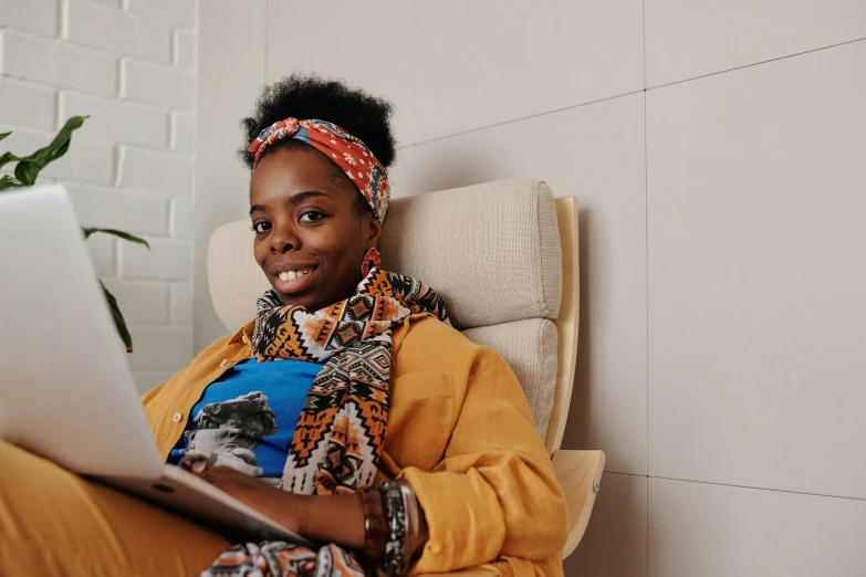 a black woman sitting on a couch looking at her laptop