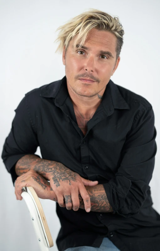 a man in black shirt sitting in chair with tattoo