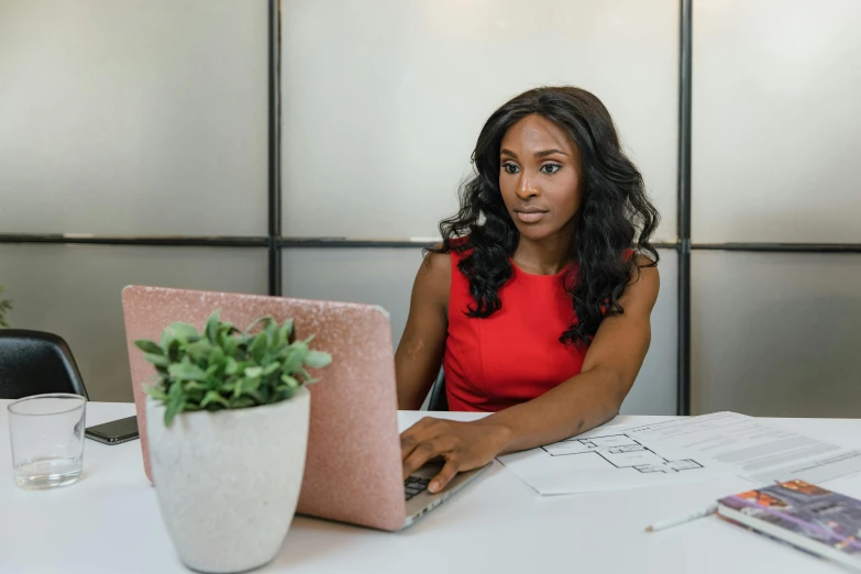 a woman in a red dress is sitting at a desk with a laptop and papers