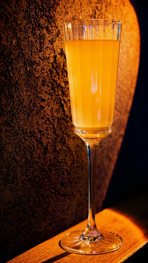 a glass of orange colored liquid sitting on a wooden table