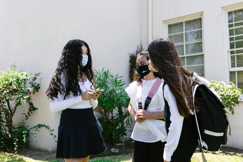 three girls wearing face masks are standing by the house
