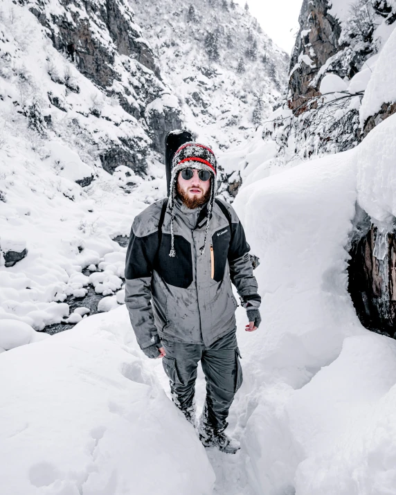 a man in grey jacket walking through snow covered mountains