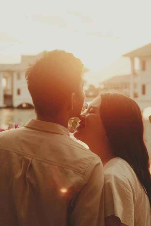 a young couple kisses in front of a sunset