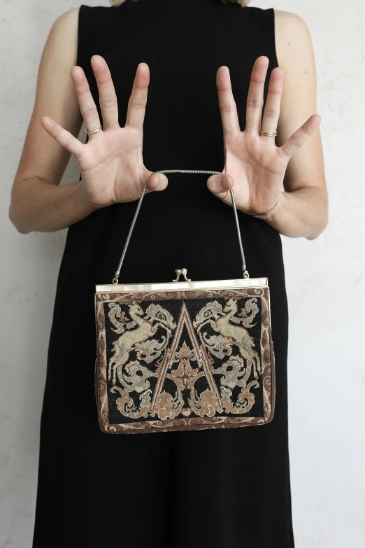 a woman wearing an ornate purse while holding up her hands