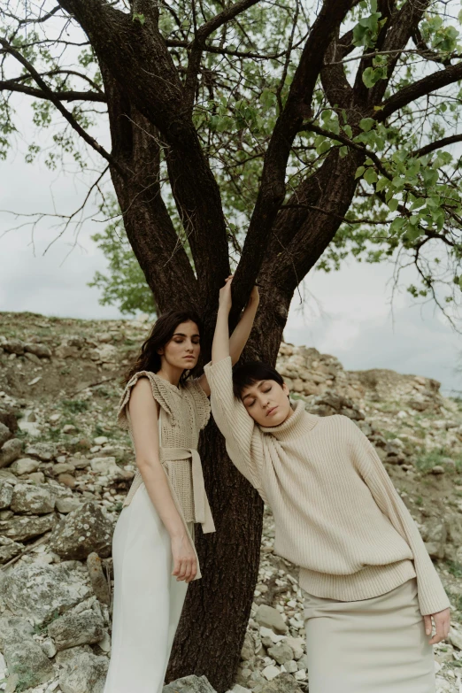 two women in dresses posing by tree with rocks