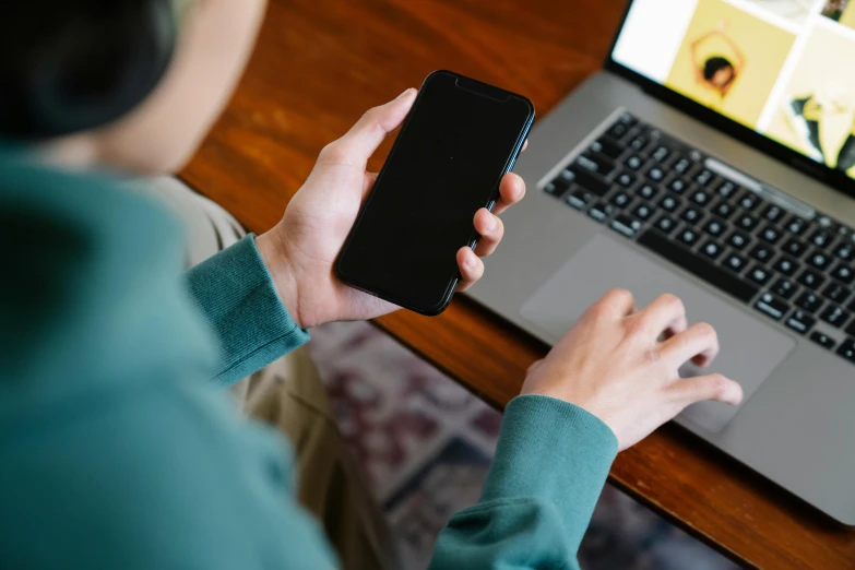 someone holding a phone over a laptop and a wooden table