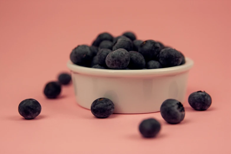 a small bowl full of ripe blackberries on a pink background