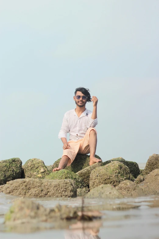 a young man in a white shirt and khaki pants poses on some rocks in the water