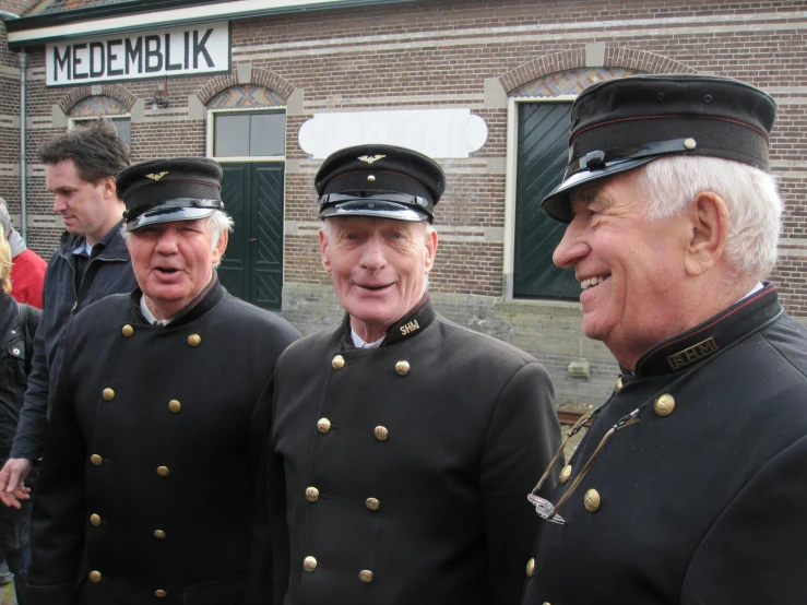 three men dressed in uniforms talking outside a brick building