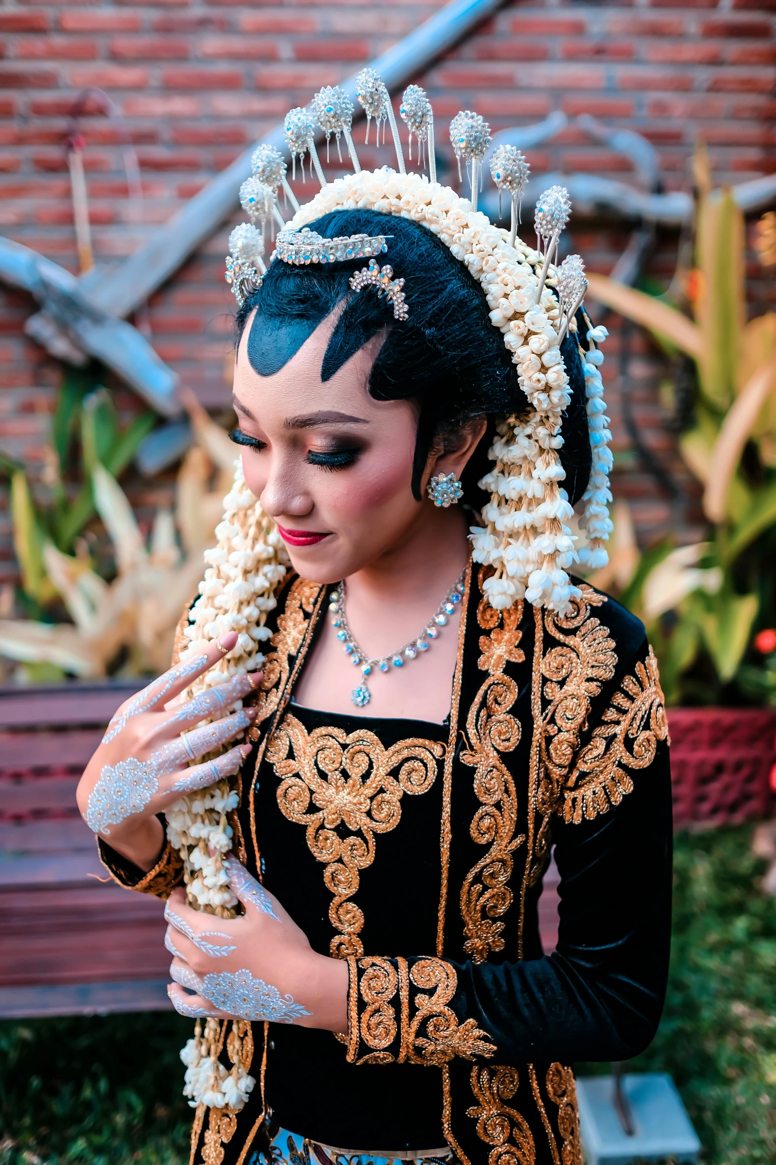 woman wearing a tiara and pearls standing in grass next to brick wall