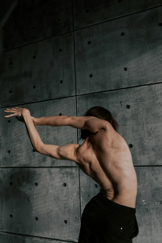 a shirtless man is dancing in front of a stone wall