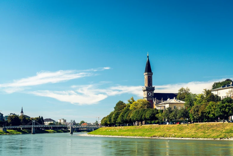 a river next to trees and buildings under a blue sky