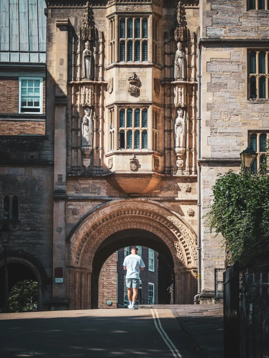 a man walking down a street in front of a stone archway