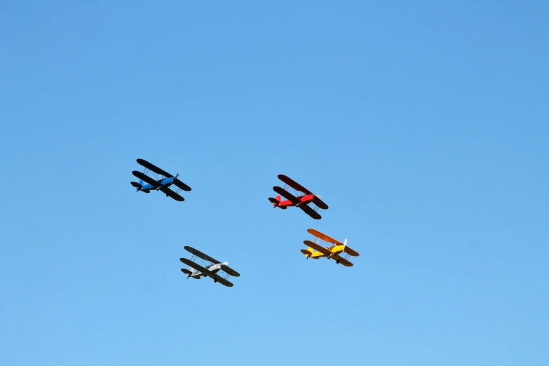 four colorful airplanes are flying in formation against a blue sky