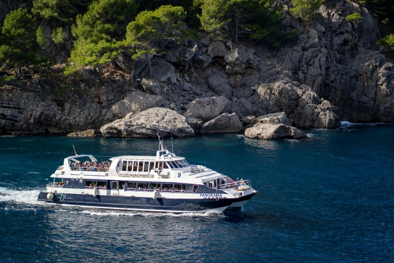 large white boat cruising along a lake near a rocky shoreline