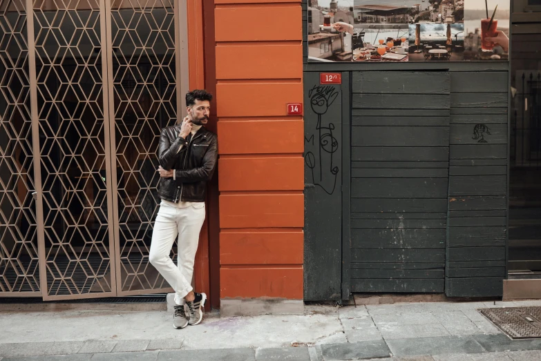 man leaning up against a store front on the phone