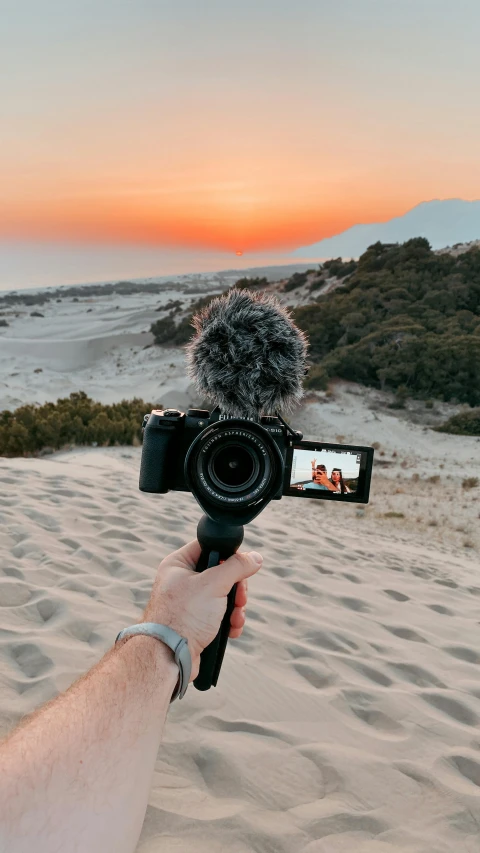 a hand holding a camera up to take a picture of the sun setting