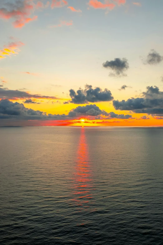 the setting sun on a calm sea with white clouds