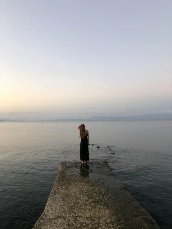 a woman stands on the edge of a jetty on a calm body of water