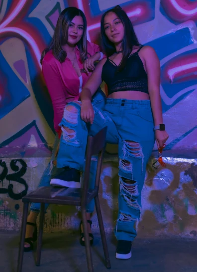 two women sitting on a stool against graffiti