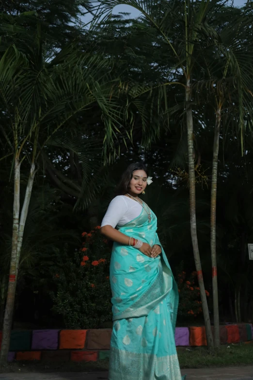 a woman poses with her hands on her hips wearing a turquoise colored saree