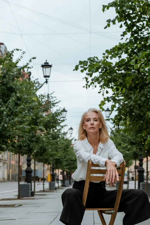 a woman is sitting on a wooden chair outdoors