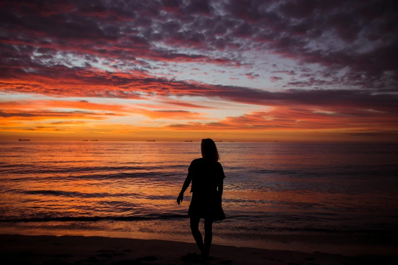 woman walking on the beach at sunset looking out to sea