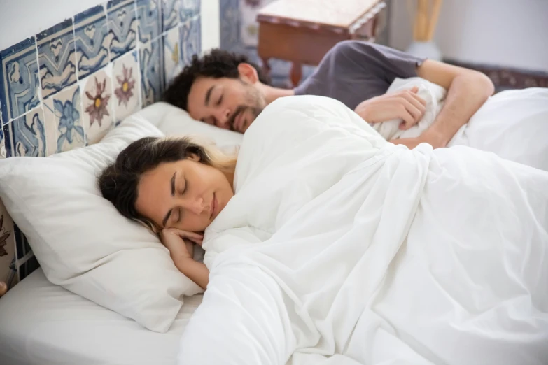 a couple sleep on the same bed as one looks at the camera