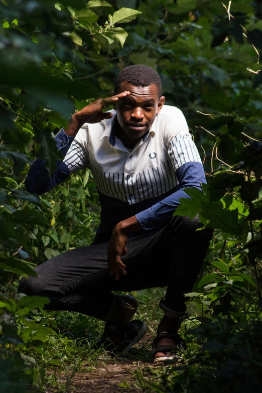 a man squatting in the woods wearing a sweater