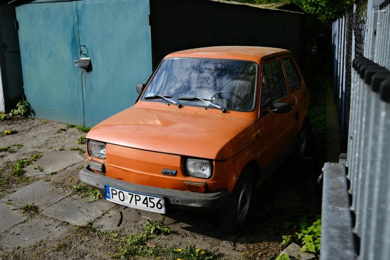 an old small orange car is parked next to a blue building
