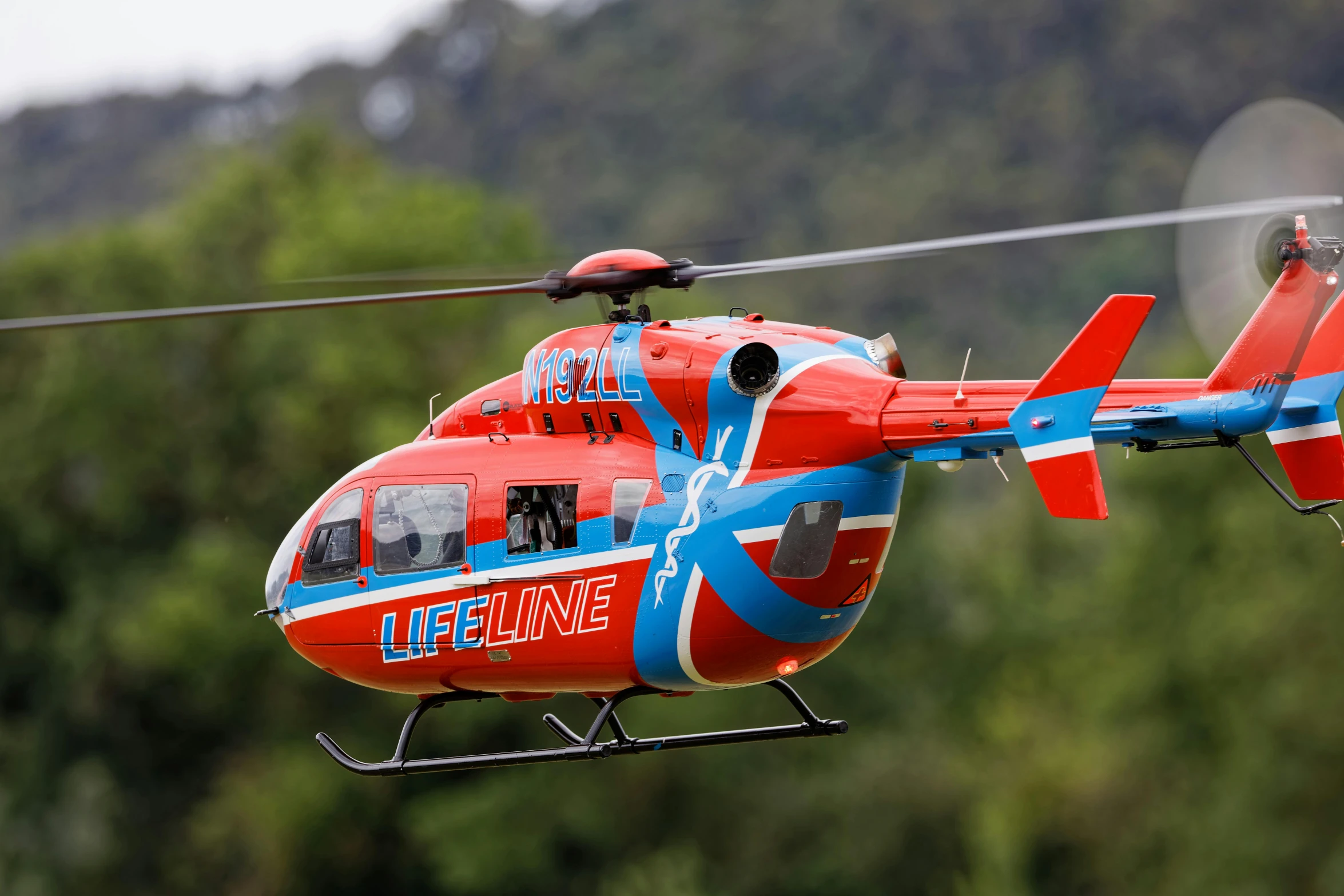 a red helicopter flying over a green forest