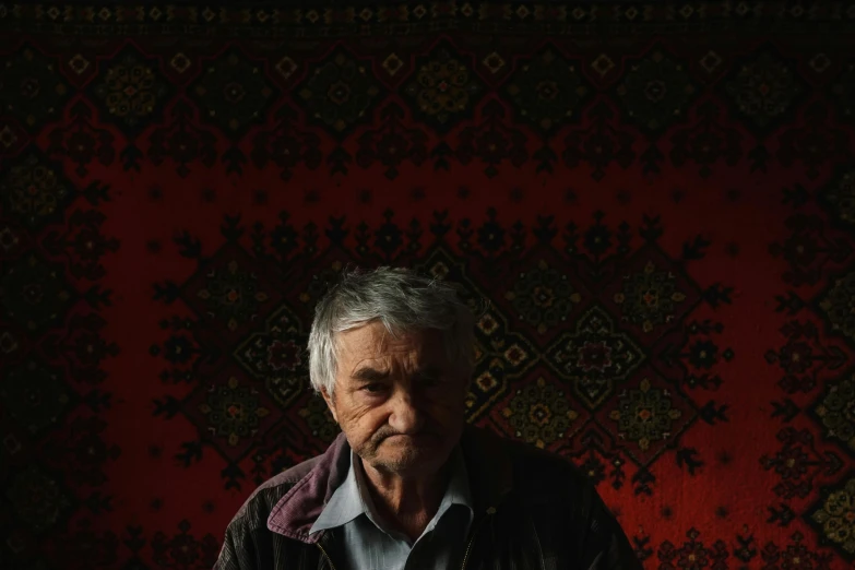 a old man is standing against a carpet