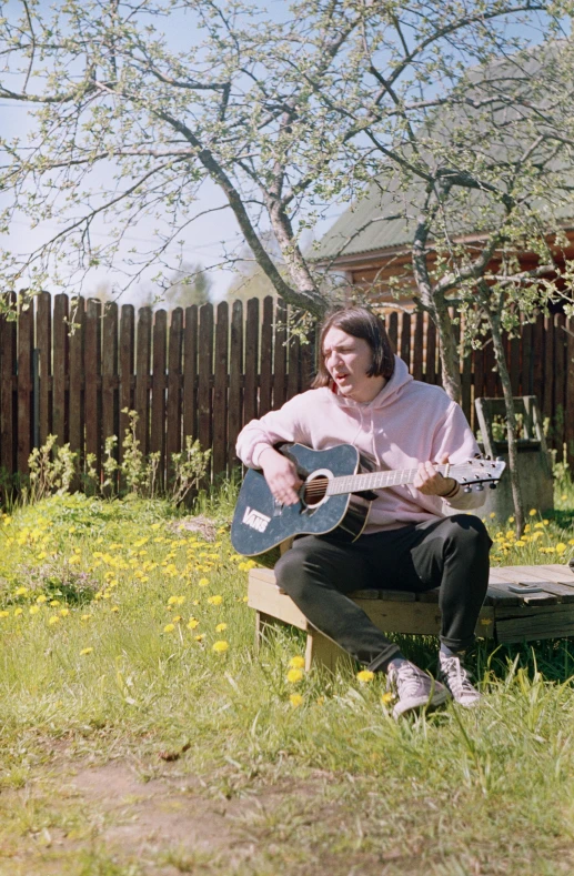 a man is sitting in the grass playing his guitar