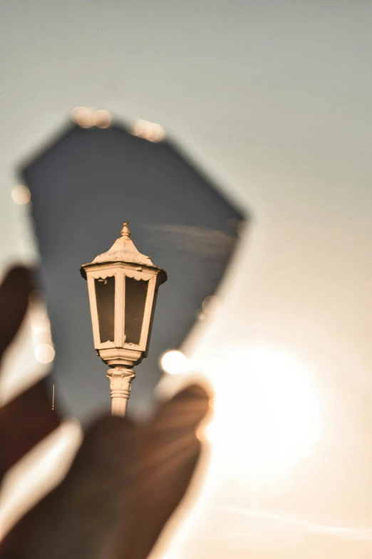 a person holding a small lantern with the sun shining behind